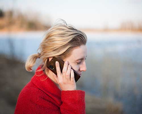 Blonde woman in red sweater talking on a cell phone outside